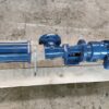 Eine blaue Fludyn BEL 1024/630 Exzenterschneckenpumpe / Monopumpe, mit Motor ausgestattet, versandfertig auf einer hellen Holzpalette verschraubt. Sie steht auf einem marmorierten Betonboden.