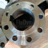Un casquillo de apriete metálico. Se apoya en la parte inferior sobre un trozo de madera. Tiene ocho orificios en la zona exterior y un orificio con un rebaje para una ranura en el centro elevado.